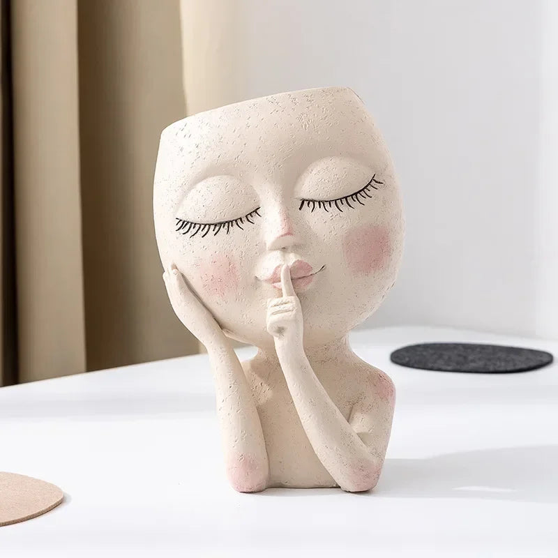 "Hush Muse" sculptural face resin planter in ivory cream, close-up detail showing hand-painted eyelashes, rosy cheeks and shh finger gesture, neutral background