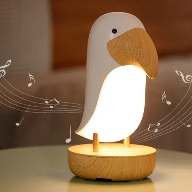 Bird-shaped LED night light glowing warm white on a bedside table, with illustrated music notes showing the built-in Bluetooth speaker