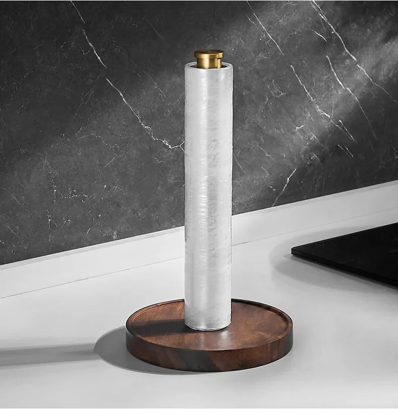 Walnut & Gold Paper Towel Holder with a plastic wrap roll on a white countertop — showing versatile use beyond kitchen paper, dark marble wall background.