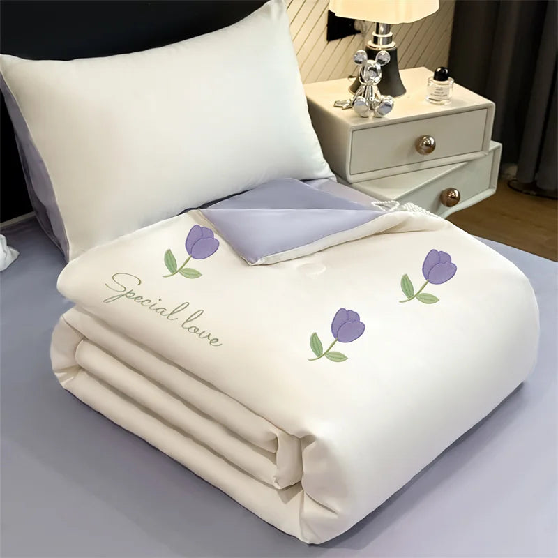 Alt text: "Ice Bloom cooling summer quilt in Lavender Tulip — ivory white with embroidered purple tulip motifs and 'Special Love' script detail, lavender grey reverse"