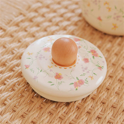Imagem 3: Close-up of floral enamel teapot lid with round wooden knob and delicate pink blossom print, resting on woven rattan surface — Blossom Kettle by CL House