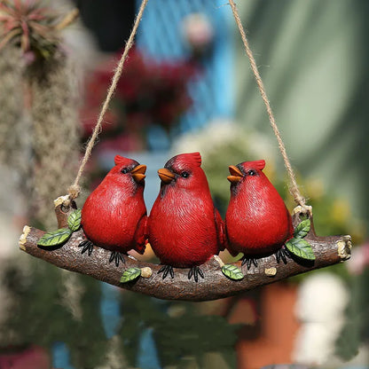 "Wild Perch" hand-painted resin red cardinal trio on hanging branch ornament with jute rope, displayed in lush garden setting with terracotta pots