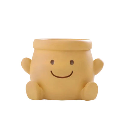 "Happy Pot" smiley face resin succulent planter in mustard yellow with open arms design and drainage hole, white background