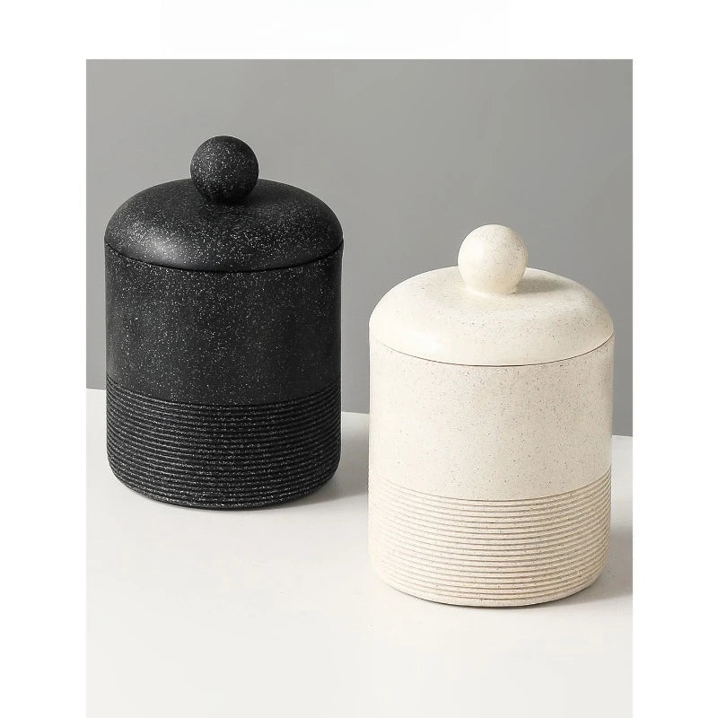 Midnight Stone and Chalk Stone ceramic storage jars with lids side by side on white surface with grey background, showing contrast between dark speckled and warm cream stone textures