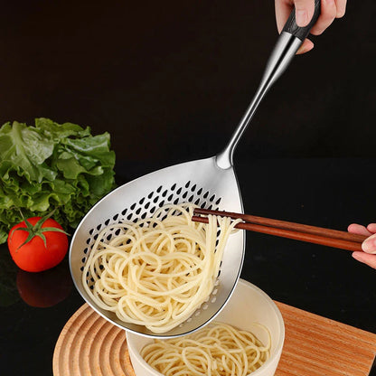 Stainless steel wok skimmer with dark wood handle draining noodles into a bowl, with fresh vegetables in the background