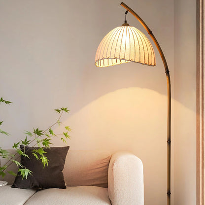 Arc & Pleat canvas floor lamp casting warm light over a cream sofa and dark cushion, with a Japanese maple plant beside it in a minimalist living room setting