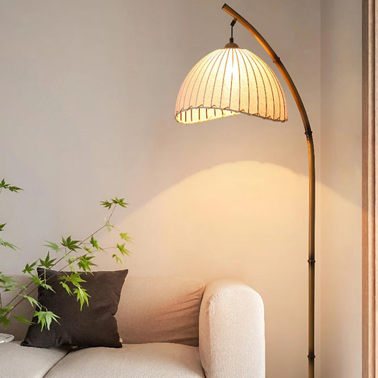 Arc & Pleat canvas floor lamp casting warm light over a cream sofa and dark cushion, with a Japanese maple plant beside it in a minimalist living room setting