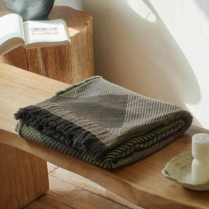  Forest Dusk 100% cotton jacquard woven throw blanket with geometric diamond pattern and dark fringe trim folded on a wooden bench in a sunlit japandi interior