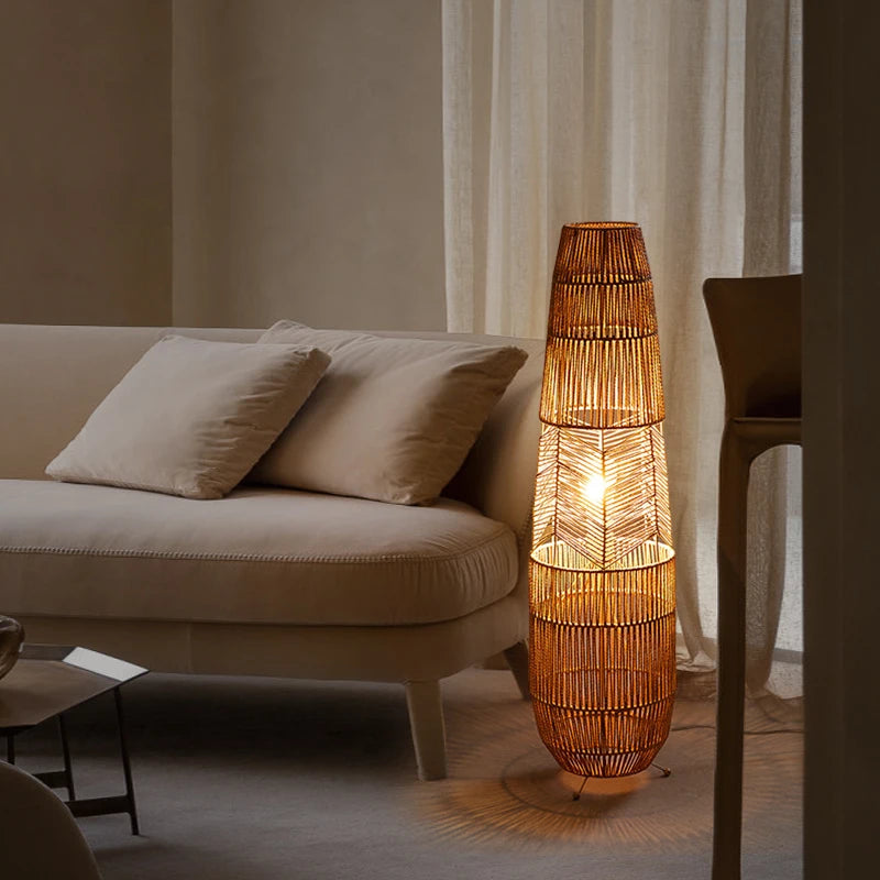 "Weave & Glow" rattan floor lamp glowing warmly beside a cream sofa in a softly lit living room with sheer curtains