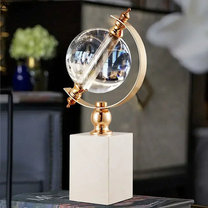 Crystal globe sculpture with gold-plated ring and white marble base, close-up lifestyle shot in dark styled interior with blurred background