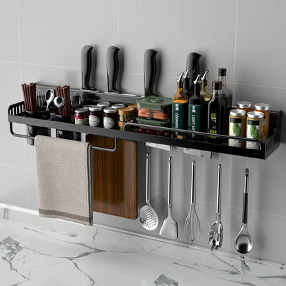 Matte black wall-mounted kitchen organiser shelf 50cm fully loaded on a grey tiled wall above a marble countertop — knives in slots, spices and condiments on shelf, single organiser cup with chopsticks, 6 hooks with spatula, whisk, ladle and tongs, chopping board and kitchen towel — lifestyle shot of the Black Rail Kitchen Organiser by CL House