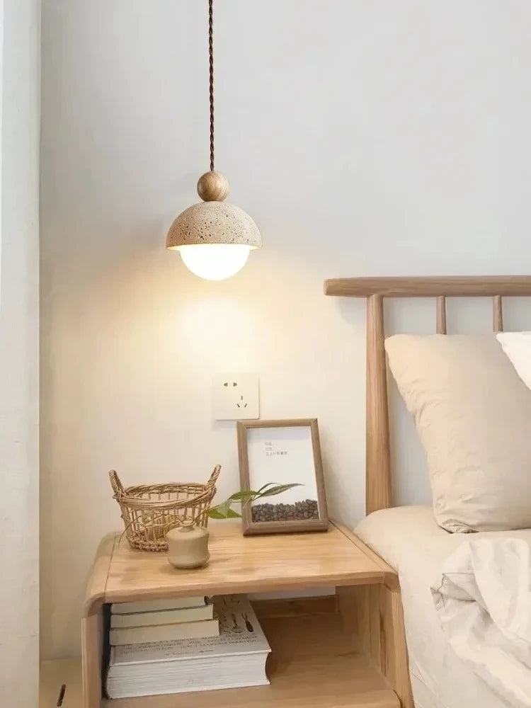  Stone & Orb travertine pendant light with log wood bead casting warm light above a wooden bedside table styled with a rattan basket, small plant and photo frame beside a natural wood bed frame
