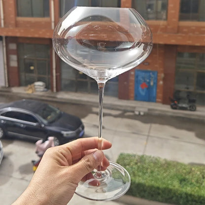 Hand holding a "Gravity" disc bowl crystal wine glass, distinctive flat disc bowl and elegant stem — CL House Drinkware collection