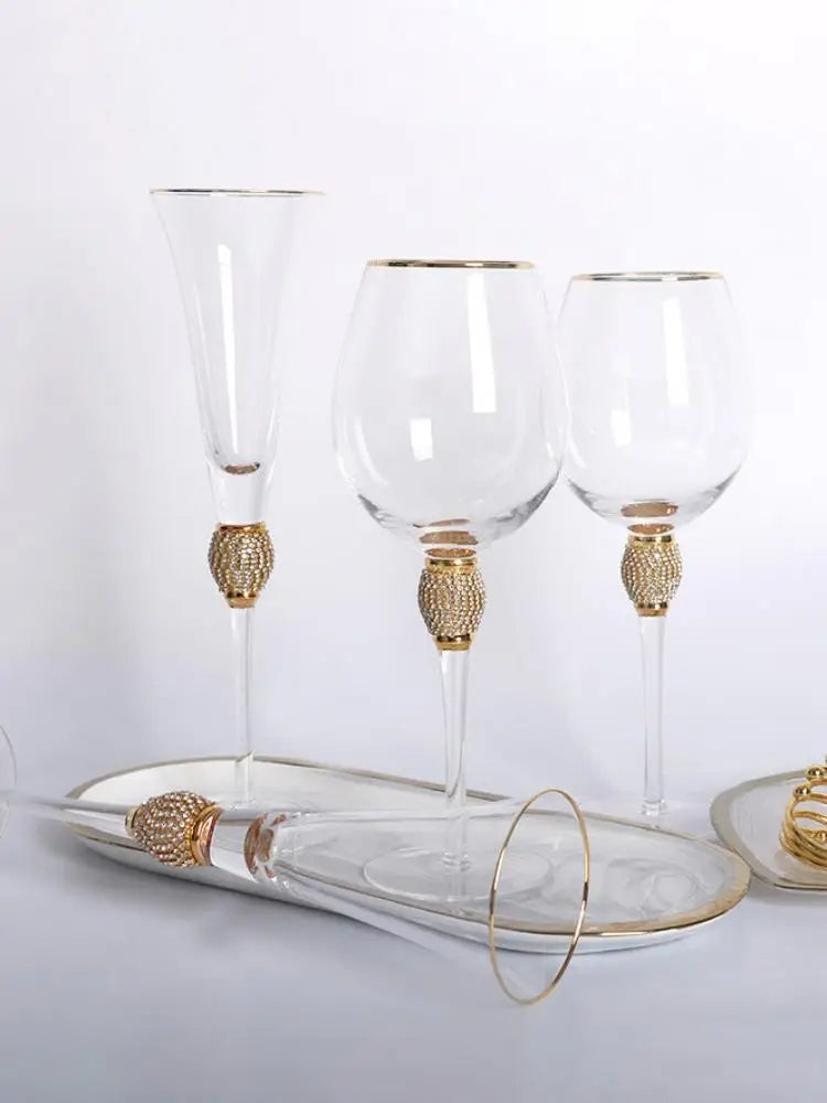 "Golden Jewel" collection — Champagne Flute, Large Wine Glass and Wine Glass with gold rim and micro-crystal bead stems, styled on a white surface with a gold-rimmed ceramic tray
