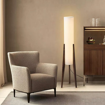  "Tripod & Cylinder" walnut floor lamp glowing warmly beside a bouclé armchair and a dark wood sideboard in a warm living room