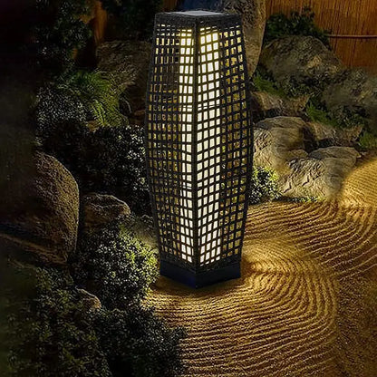  Dark wicker solar floor lantern glowing with warm white light in a zen garden with raked sand and stone landscaping at night