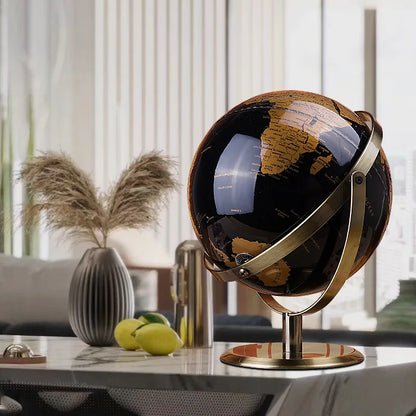Decorative world globe with black and gold vintage map on gold-plated stand, styled on marble coffee table with pampas grass vase in a bright modern living room

