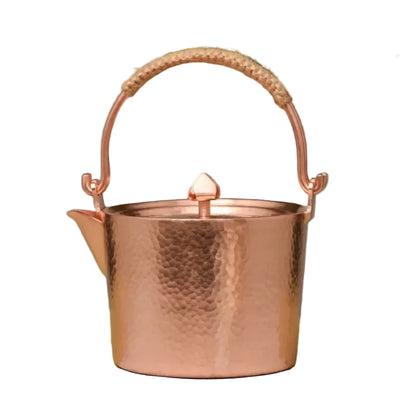 Copper Ritual handmade pure copper teapot kettle in Rose Gold finish on white background, showing the hammer-textured body, jute-wrapped arched handle and pointed lid knob