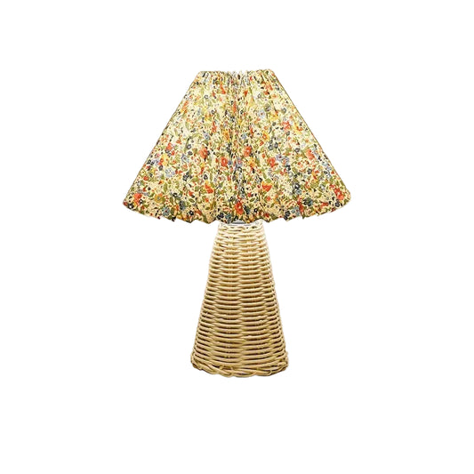  Rattan & Pleat table lamp with woven rattan cone base and pleated floral shade in red, orange and green botanical print, warm light on a white surface against a taupe wall