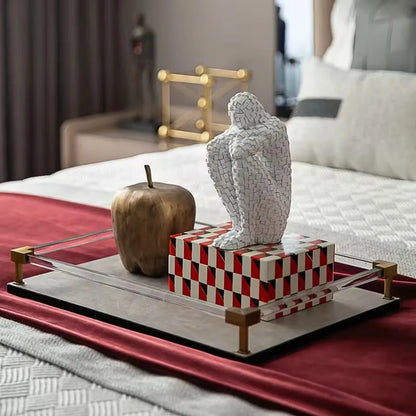 White mosaic resin figure sculpture styled on a red and black decorative book tray beside an apple in a bedroom.