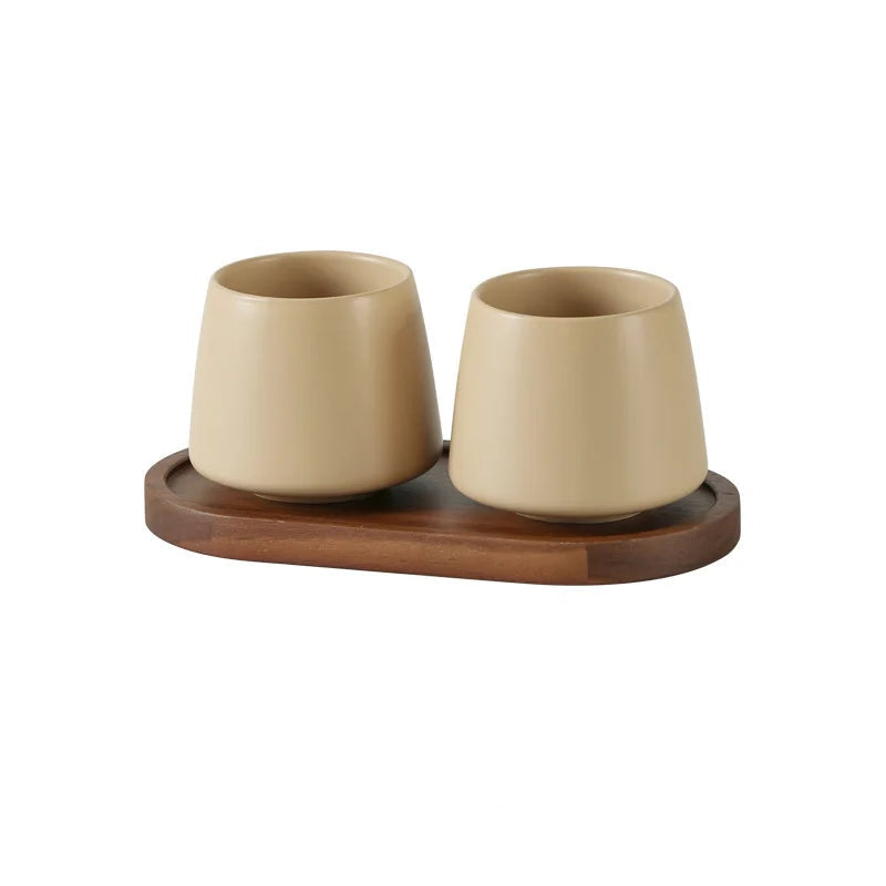 Two cone-shaped matte oat white ceramic cups on oval acacia wood tray, warm beige finish, bathroom toothbrush holder set, white background