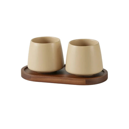 Two cone-shaped matte oat white ceramic cups on oval acacia wood tray, warm beige finish, bathroom toothbrush holder set, white background