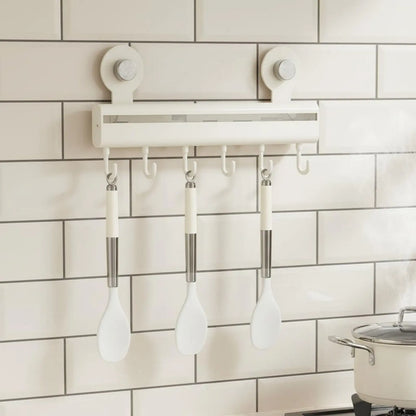 Cream adhesive wall-mounted kitchen hook rail with seven sliding hooks holding white silicone spoons on white subway tiles with a stainless steel pot on the hob below, CL House & Home