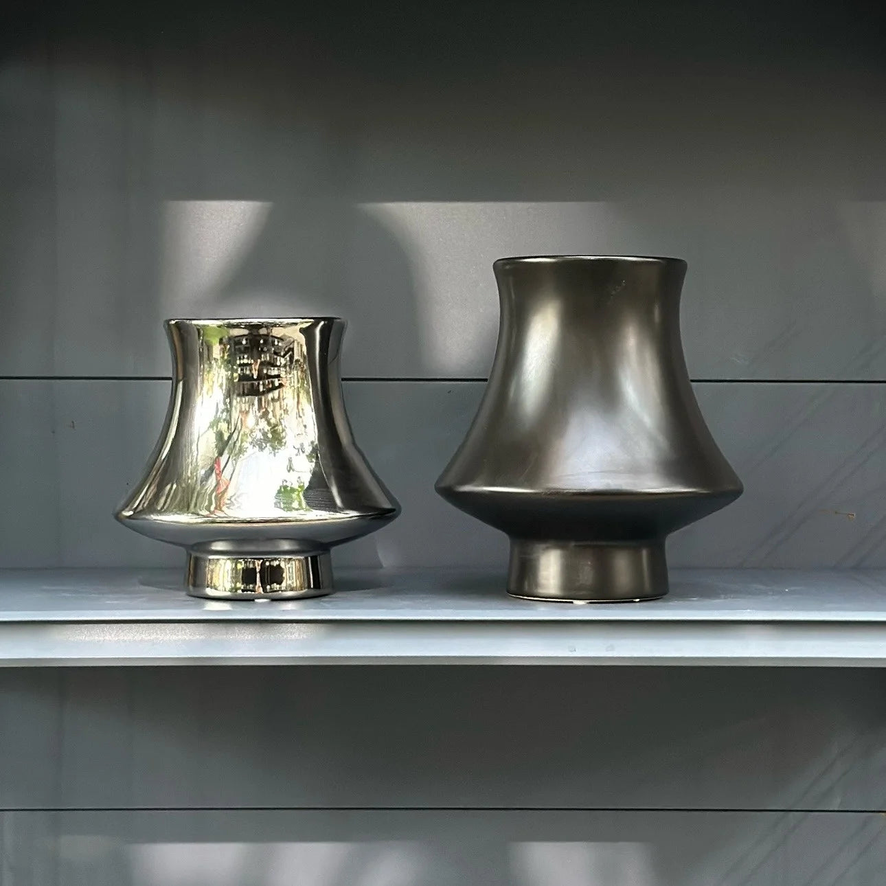 Bell Tower metallic ceramic vases in Silver Small and Gunmetal Large side by side on grey shelf, showing finish contras