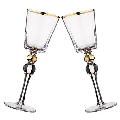 Two "Golden Hour" crystal wine glasses touching rims in a toast, gold filigree detail catching the light — CL House Drinkware collection