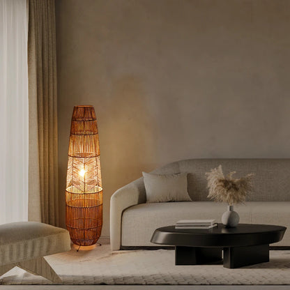 "Weave & Glow" rattan floor lamp casting warm golden light in a minimalist living room with a beige sofa, dark coffee table, and pampas grass vase