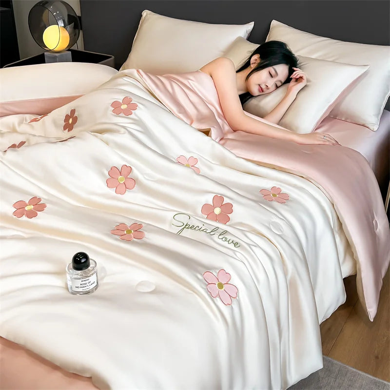 "Ice Bloom cooling summer quilt in Blossom Pink — woman sleeping under lightweight ivory white quilt with embroidered pink daisy motifs, blush pink reverse, cool and breathable summer bedding"