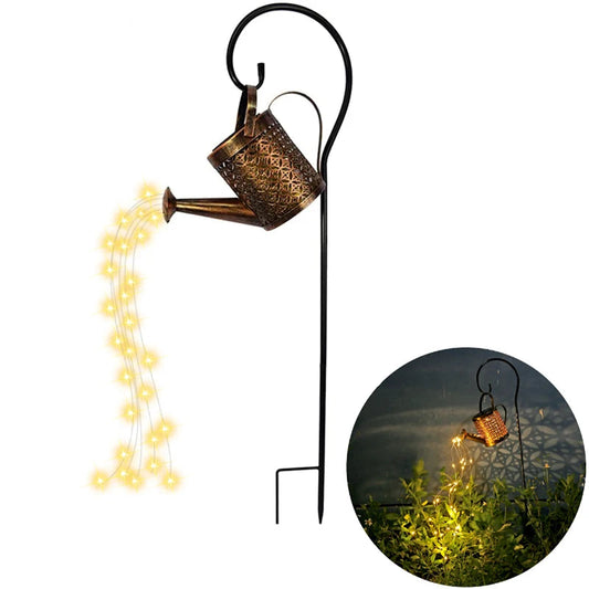 Starfall Kettle" solar fairy light watering can, Lattice Copper finish with geometric filigree pattern, mounted on black shepherd's hook pole, warm LED fairy lights cascading from spout, shown on white background with night garden inset