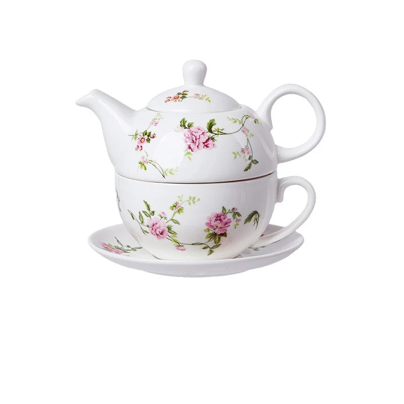 White porcelain tea for one set with delicate pink peony flowers and green trailing vines, teapot stacked on cup and saucer on white background