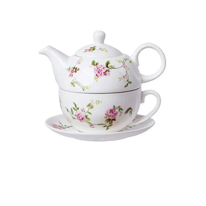 White porcelain tea for one set with delicate pink peony flowers and green trailing vines, teapot stacked on cup and saucer on white background