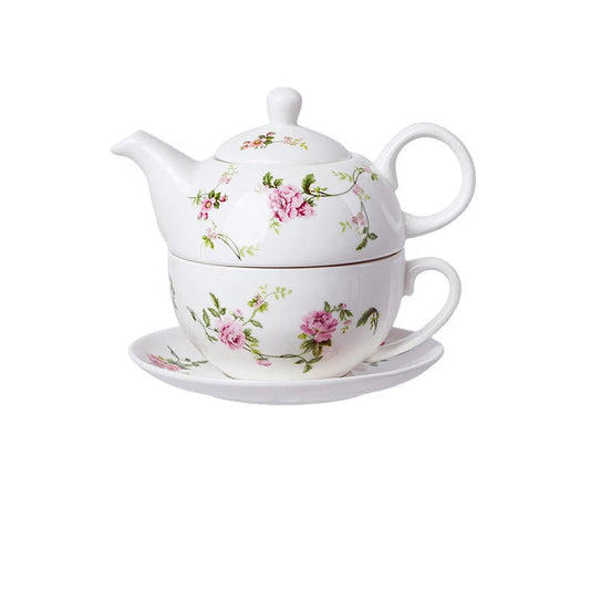 White porcelain tea for one set with delicate pink peony flowers and green trailing vines, teapot stacked on cup and saucer on white background