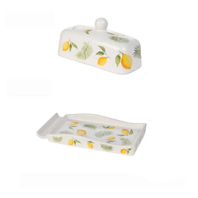 Lemon-patterned ceramic butter dish shown disassembled — domed lid and rectangular tray displayed separately on a white background, showing the full design detail.