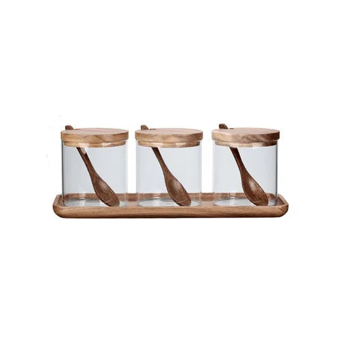  Set of three clear glass spice jars with acacia wood lids and matching wooden spoons, displayed on a rectangular acacia tray, white background — Acacia & Glass Spice Jar Set by CL House
