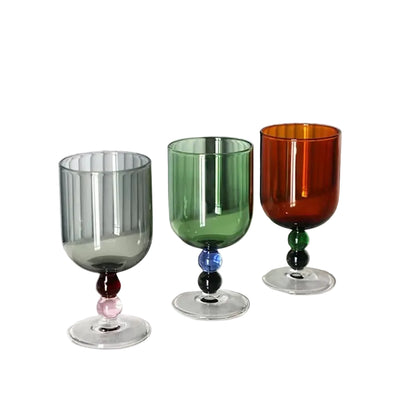 "Chromatic Orb" glass goblets in all three colours — smoke grey, forest green and amber — with contrasting two-tone bead stems, on a white background