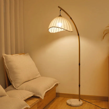 Arc & Pleat canvas floor lamp with marble base casting warm ambient light beside a low linen daybed with cream cushions, next to sheer curtains in a serene bedroom setting