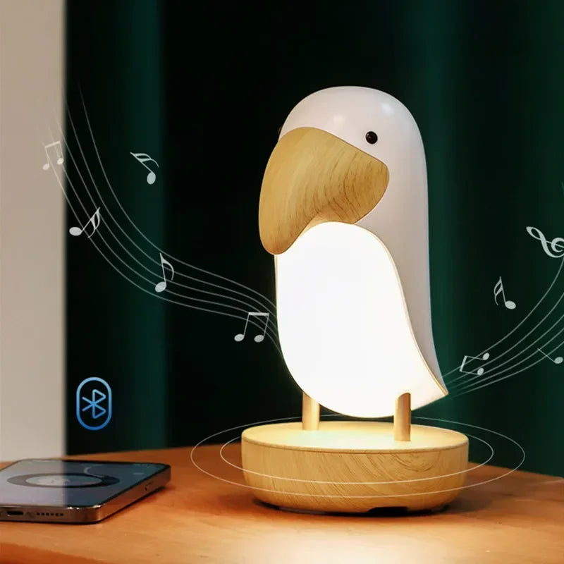 : Birdie LED night light on a wooden desk next to a smartphone, with Bluetooth icon and music notes showing wireless speaker connectivity against a dark green background