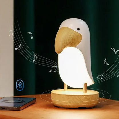 : Birdie LED night light on a wooden desk next to a smartphone, with Bluetooth icon and music notes showing wireless speaker connectivity against a dark green background