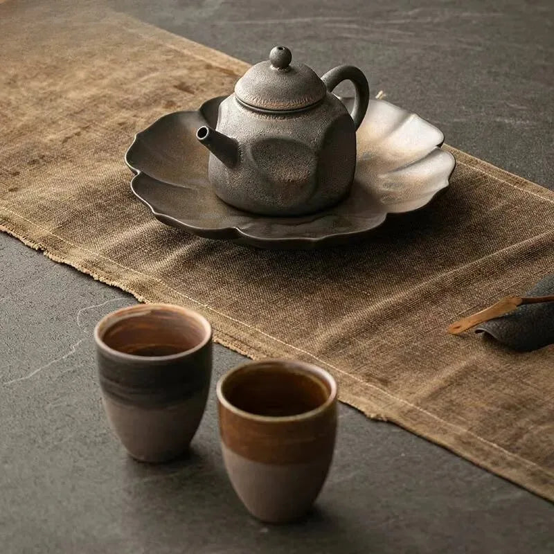 Five wabi-sabi petal ceramic dishes in charcoal and ivory arranged with fruit and food on a dark linen surface