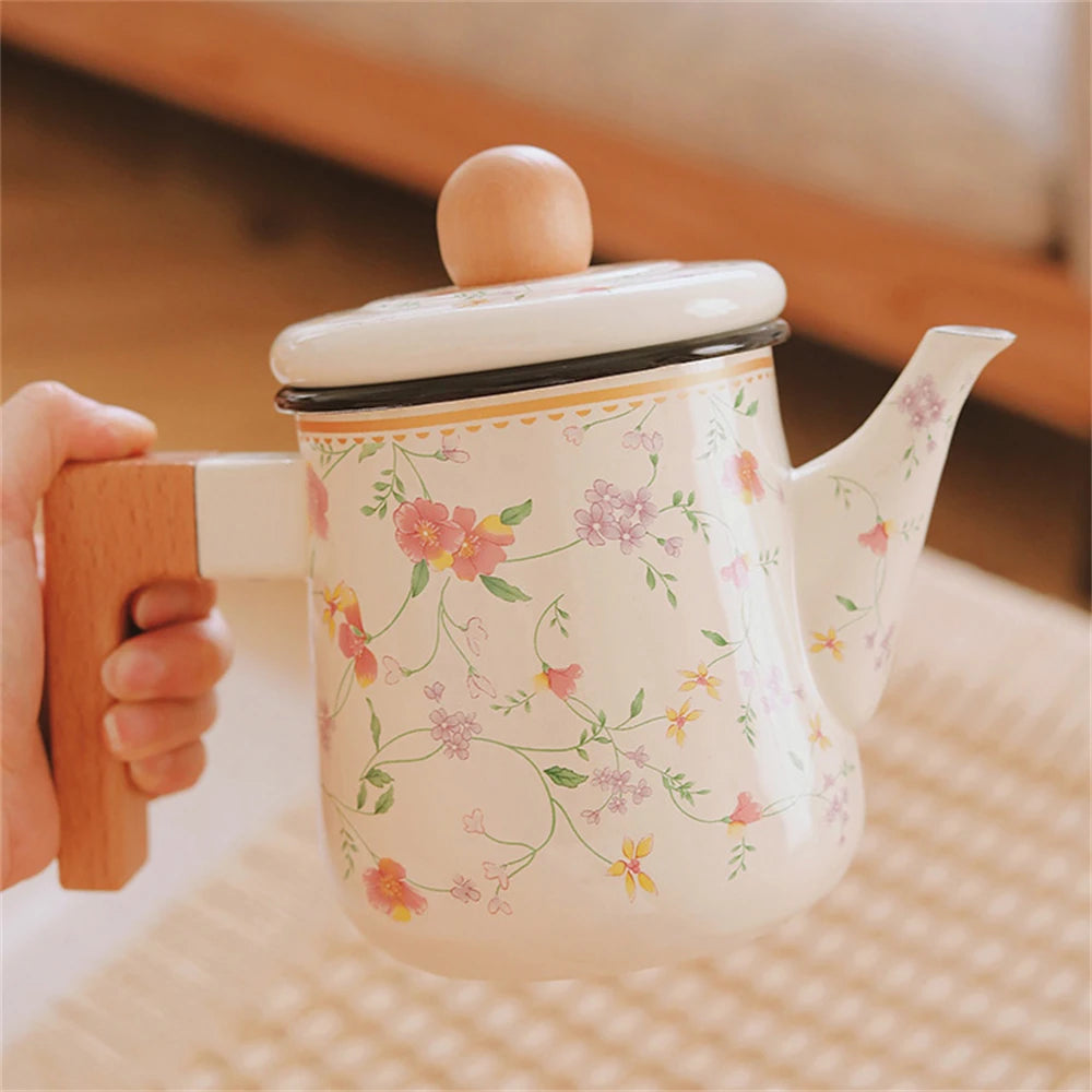 Hand holding a floral enamel teapot with wooden handle, showing pink and lilac blossom print detail — Blossom Kettle by CL House