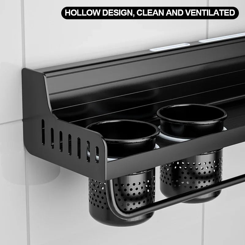 Underside close-up of matte black kitchen shelf showing hollow ventilated design of two organiser cups and perforated drip baskets below — space aluminium construction with slotted side panels and towel bar rail