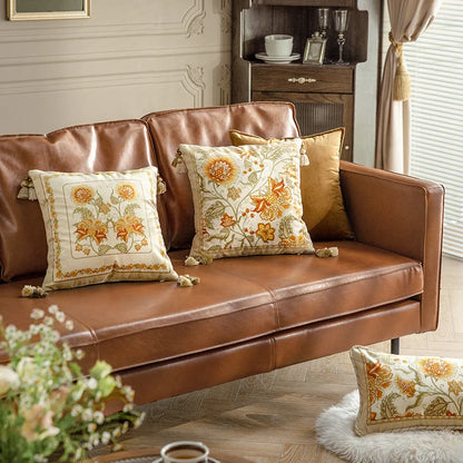  "Golden Frame" and "Wild Harvest" floral embroidered cushion covers styled on a brown leather sofa with gold velvet cushions, amber botanical motifs on ivory velvet — CL House Cushions collection
