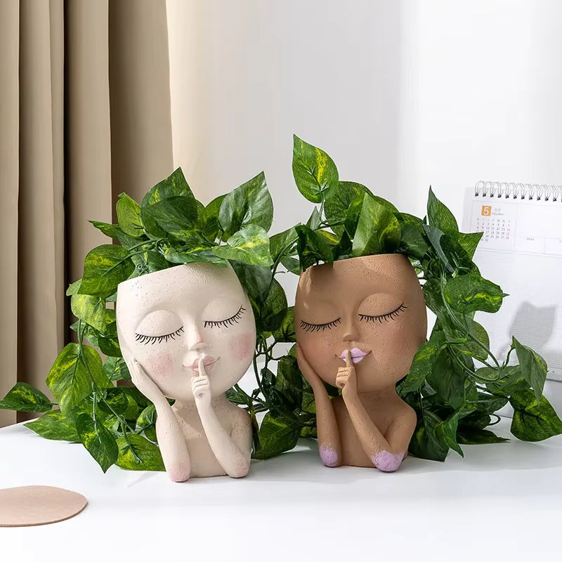 "Hush Muse" sculptural face resin planters in ivory cream and terracotta rose displayed side by side with cascading golden pothos plants, showing both colour variants with hand-painted detail