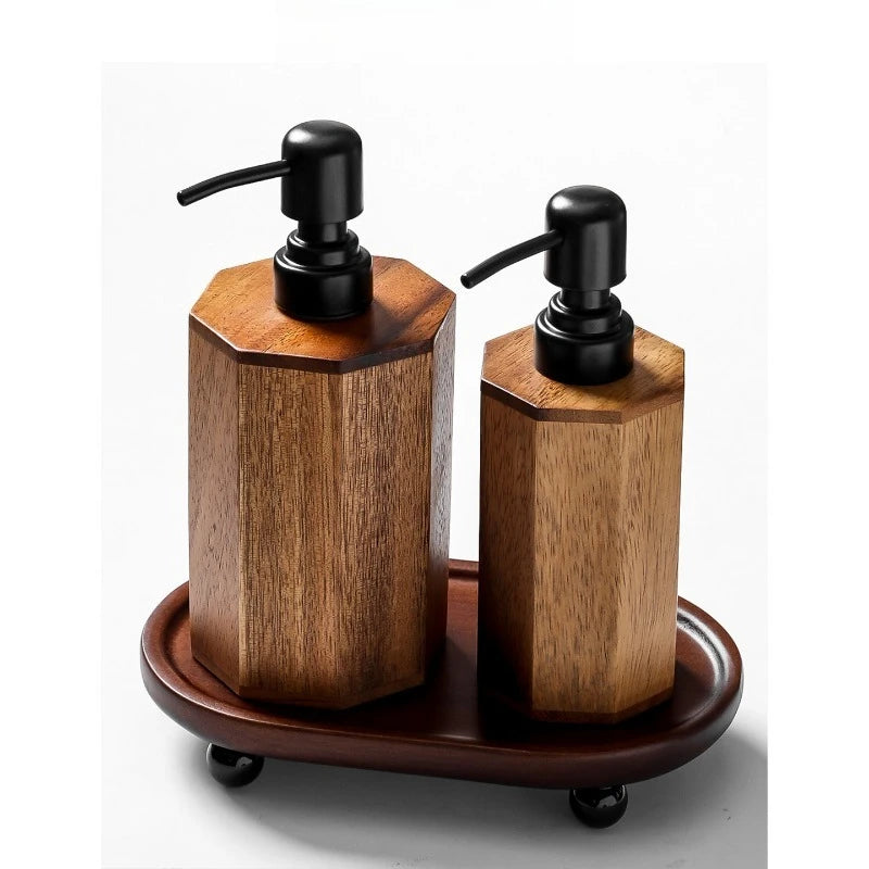 Two octagonal acacia wood soap dispensers with matte black pumps displayed on an oval acacia wood tray with black ball feet, warm walnut finish, white background