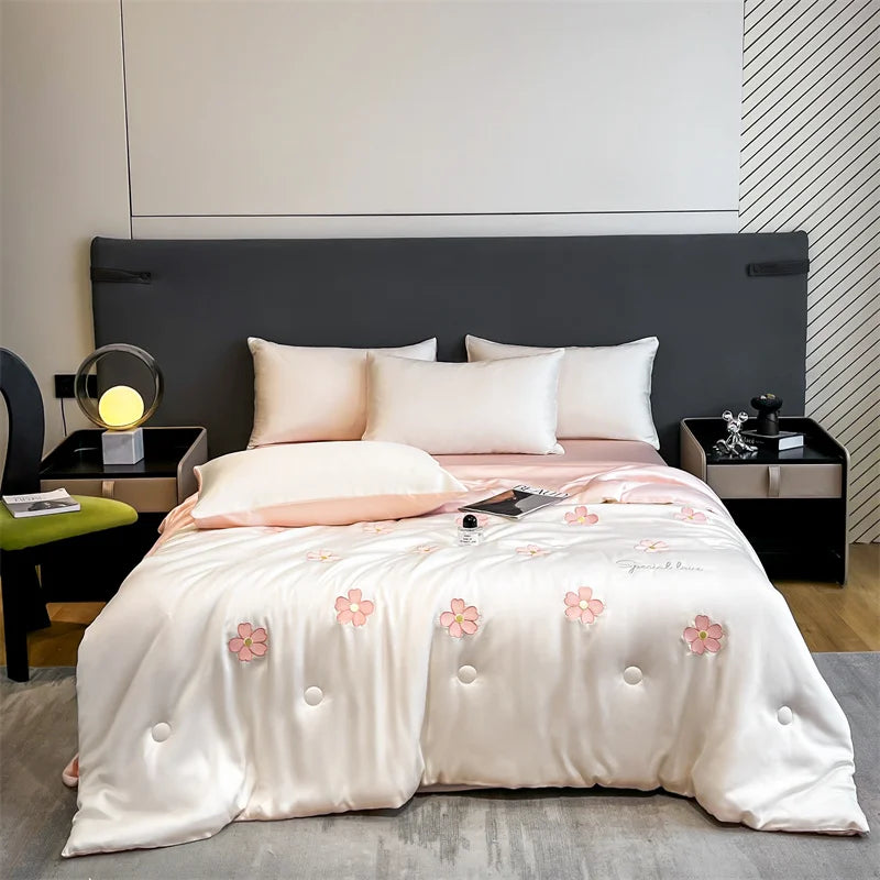 "Ice Bloom cooling summer quilt in Blossom Pink styled in a modern bedroom — ivory white with embroidered pink daisy motifs and blush pink reverse, shown on a double bed with matching pillows"