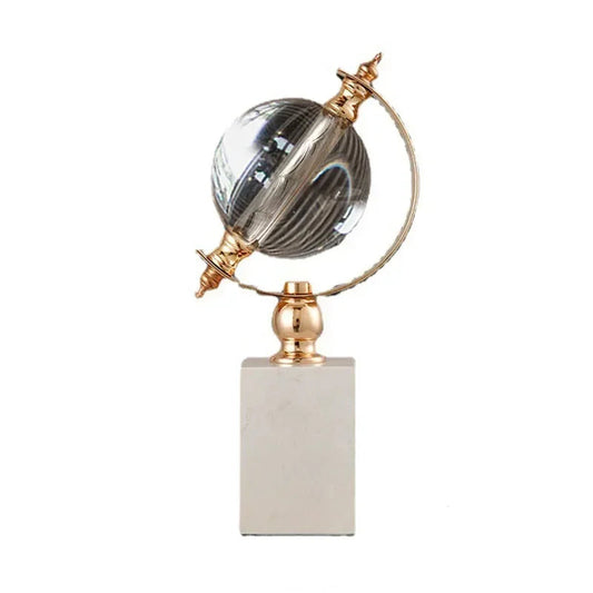 Crystal globe sculpture with gold-plated ring and white marble base, displayed inside a natural wood shelving unit