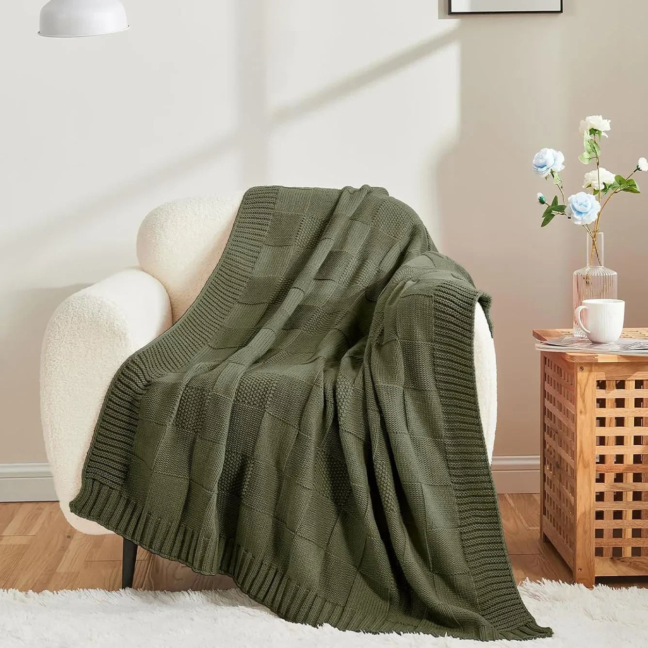 Chunky patchwork knit throw blanket in Forest Olive draped over a white bouclé armchair in a warm Scandinavian-inspired living room